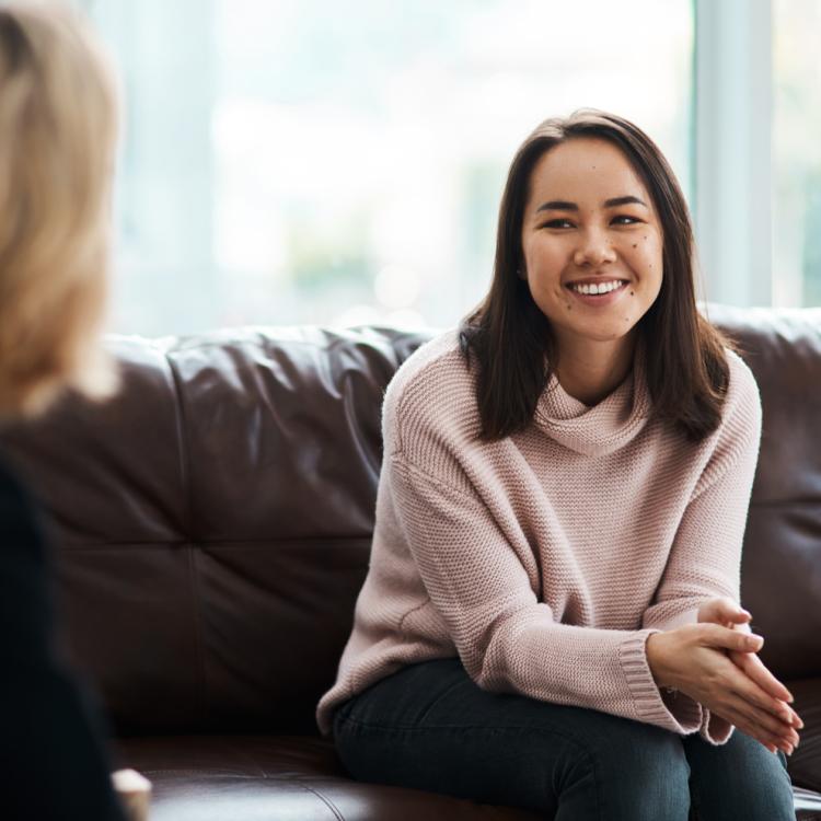 A woman in a pink sweater sits on a brown leather couch.